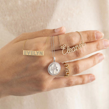 Hand wearing gold and silver jewelry with 'Evelyn' on a neutral background