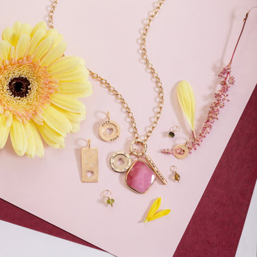 Gold necklace with pink pendant and yellow flowers on a pink background