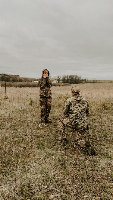 Two people in camouflage gear in a field on an overcast day