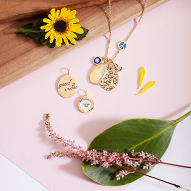 Gold necklaces with charms on a pink surface with flowers and leaves.
